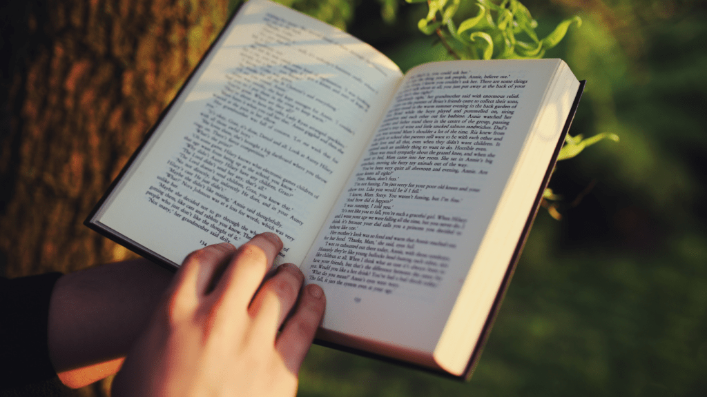 a person holding an open book in front of a tree