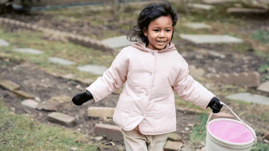 a child in a pink coat holding a bucket of pink paint