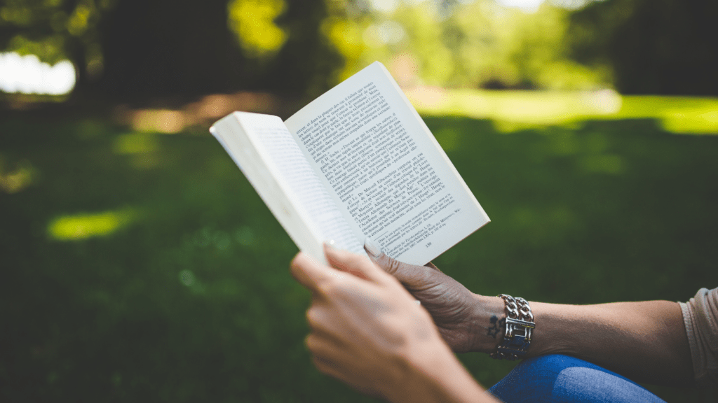 a person holding an open book in front of a tree